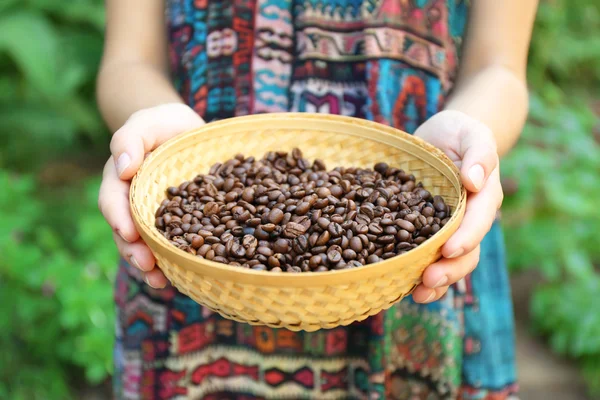 Woman holds in hands wattled basket with roasted coffee beans