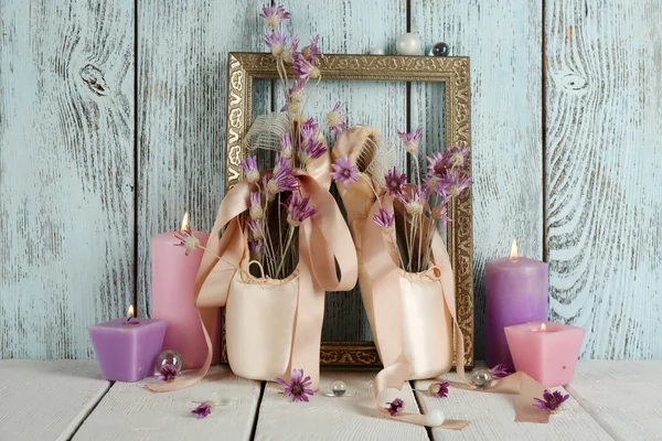 Decorated with flowers and candles ballet shoes in frame on blue wooden background