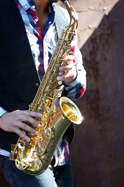 Handsome young man with sax on old brown wall background, close up