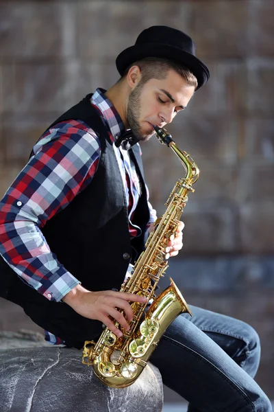 Handsome young man plays sax on stone wall background