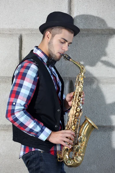 Handsome young man with sax on brick wall background