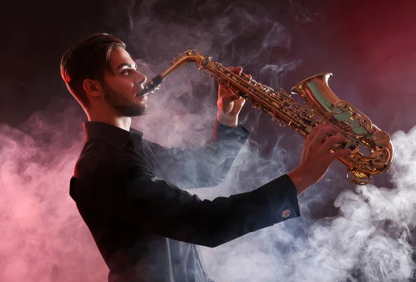Young man professionally plays sax in red smoke