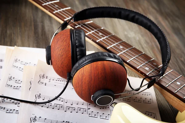 Electric guitar with headphones and musical notes on wooden background