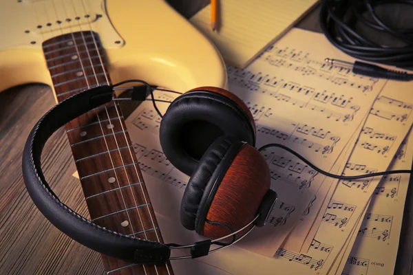 Electric guitar with headphones and musical notes on wooden background