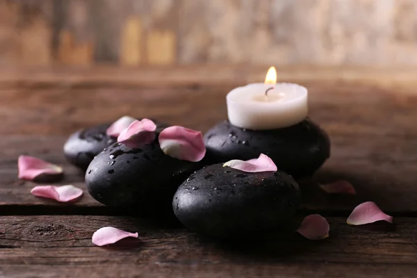 Alight candle and pebbles covered with rose petals on wooden background