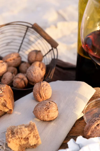 Beautiful romantic composition of red wine, bread and nuts on sandy beach, close up