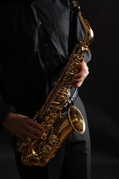 Musician in black shirt with sax on dark background, close up