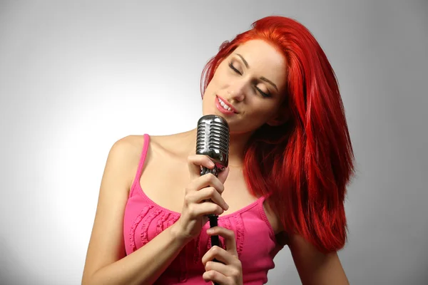 Beautiful young woman with microphone on gray background