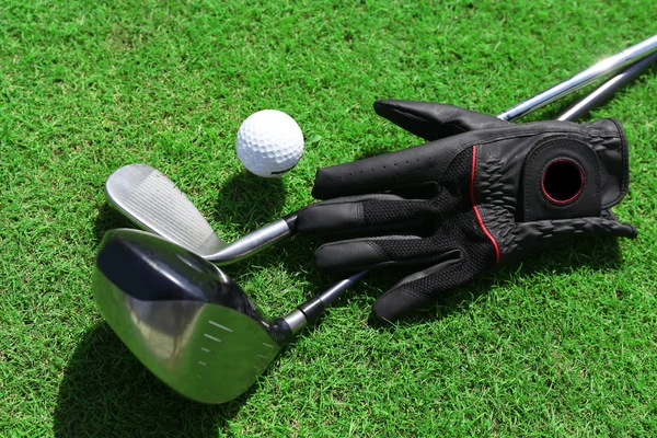 Golf clubs with ball and black glove on a green grass, close up