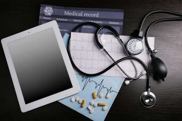 Blood pressure meter, stethoscope, digital tablet on dark background