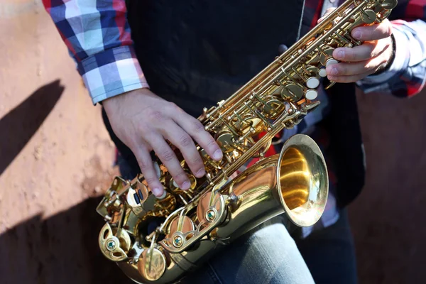 Handsome young man with sax on old brown wall background, close up