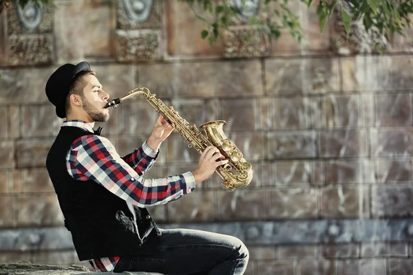 Handsome young man plays sax on stone wall background