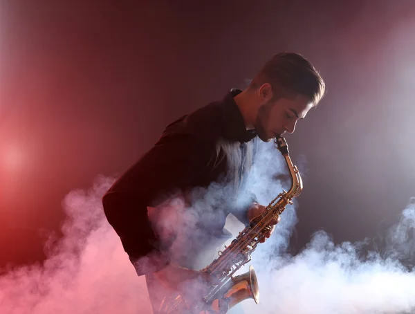 Young man professionally plays sax in red smoke