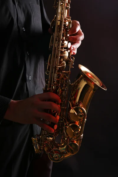 Musician in black shirt with sax on dark background, close up