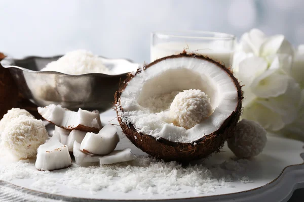 Candies in coconut flakes and fresh coconut on color wooden background