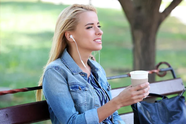 Young woman sitting on bench and  listening to music in the park