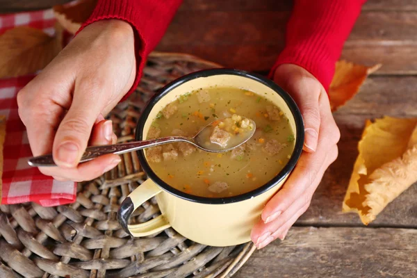 Woman hands holding a mug of soup on wicker mat on a table