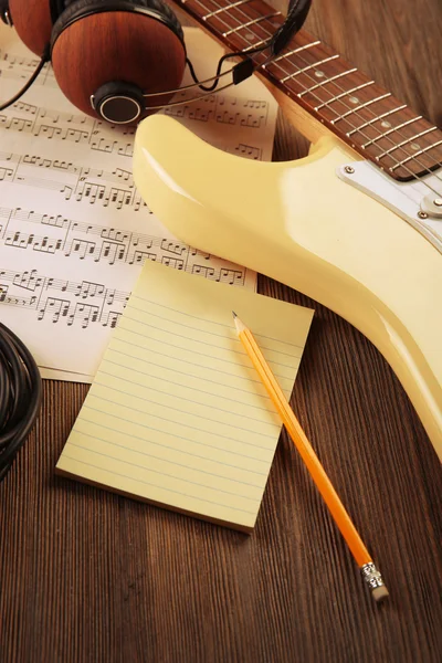 Electric guitar with headphones and musical notes on wooden background