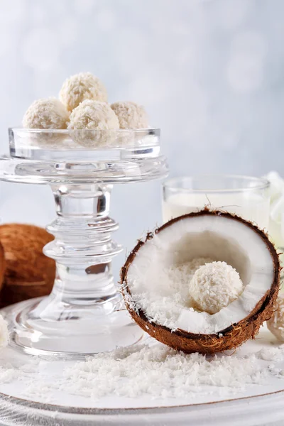 Candies in coconut flakes and fresh coconut on color wooden table, on light background
