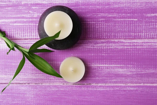 Spa composition of candles, stone and leaves on purple wooden background