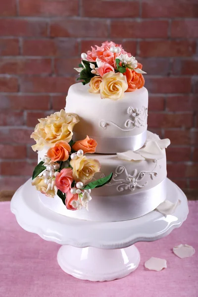 Beautiful wedding cake decorated with flowers on pink table against brick wall background