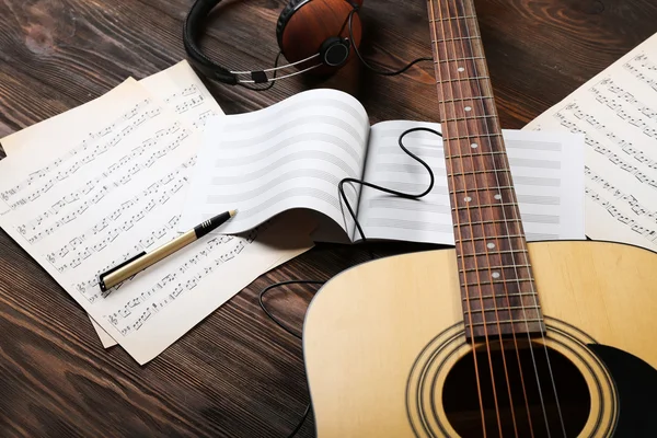 Guitar with earphones and music sheets on wooden background