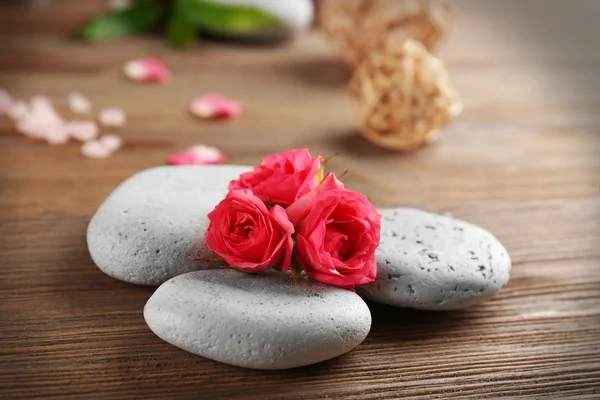 Alight wax grey candles with roses and pebbles on wooden background - relax concept