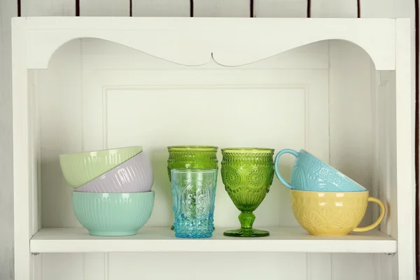 Clean glasses, plates and cutlery on shelf in kitchen cupboard