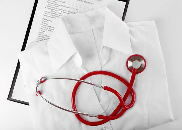 Stethoscope, medical record and uniform on white background