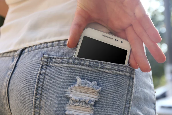Female hand puts white smart mobile phone into jeans pocket