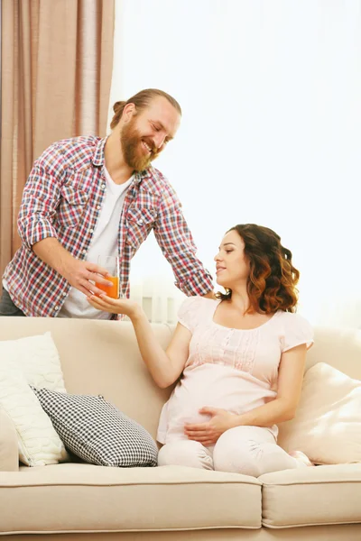 Handsome man gives a glass of juice to his lovely pregnant woman
