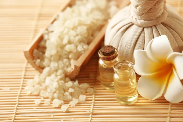 Spa set with massage balls, salt, aroma oil and frangipani flower on wicker background