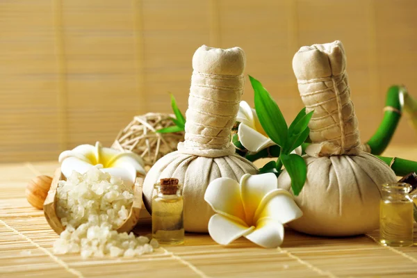 Natural spa set with massage balls, salt, aroma oil and frangipani flower with bamboo on wicker background