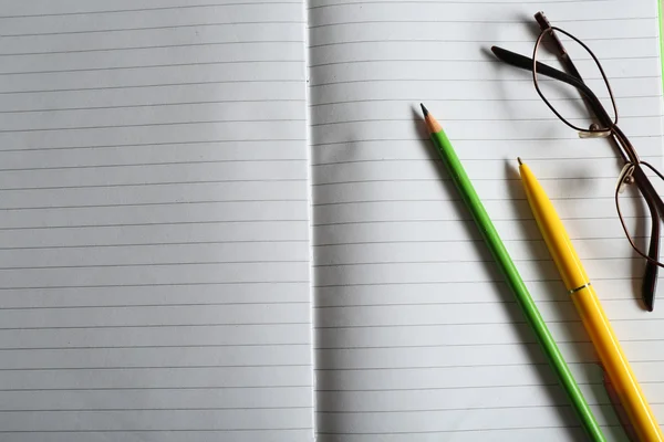 Opened striped note book background with yellow pen and green pencil