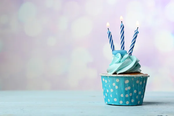 Sweet cupcake with candles on blue wooden table against blurred background