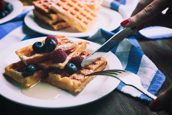 Woman eating Sweet homemade waffles with forest berries and sauce, close-up