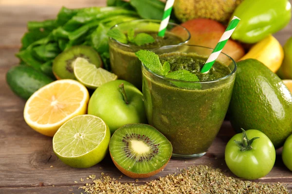 Green healthy juice with fruits and vegetables on wooden table close up