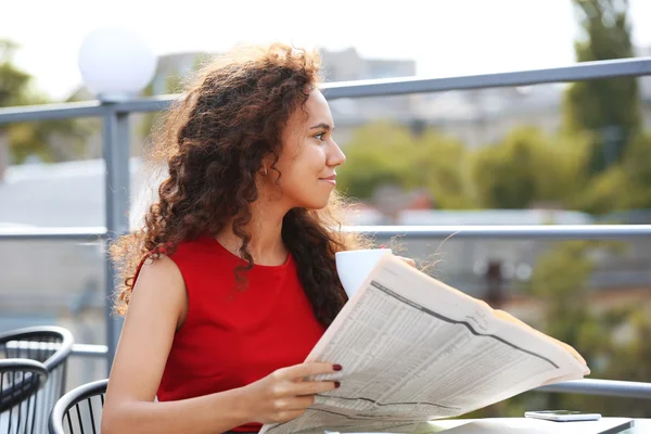 Young pretty business woman in red dress reads newspaper at the restaurant\'s terrace