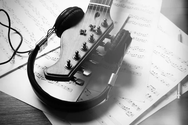 Neck of acoustic guitar with headphones and music notes on table, close-up