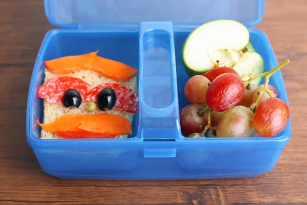 Creative sandwich and fruits in plastic lunchbox on wooden background