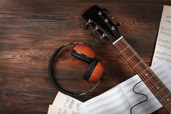 Guitar with earphones and music sheets on wooden background