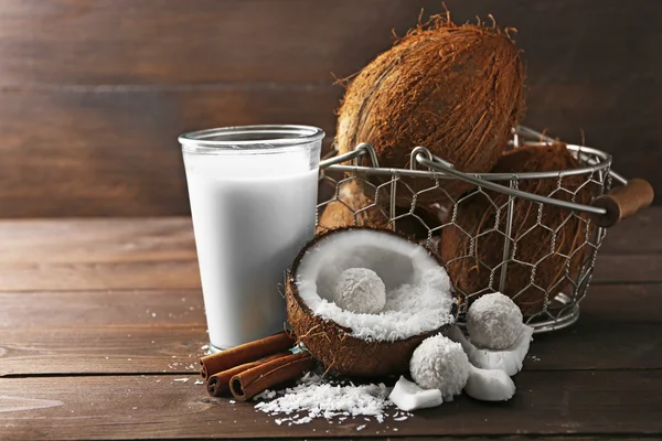 Candies in coconut flakes, glass of milk and fresh coconut on dark wooden background