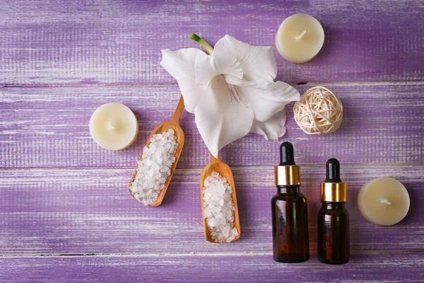 Spa composition of candles, oil, sea salt and flower on purple wooden background