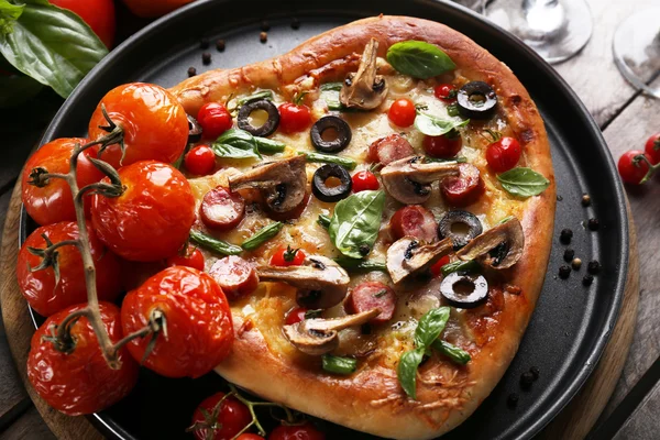 Decorated pizza with vegetables on pan on wooden background