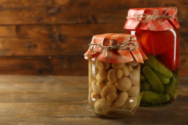 Jars with pickled vegetables and mushrooms on wooden background