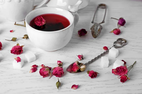 Tea and tea rose flowers on table