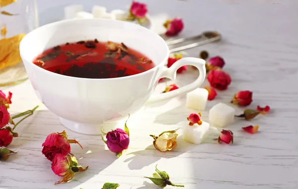 Tea and tea rose flowers on table