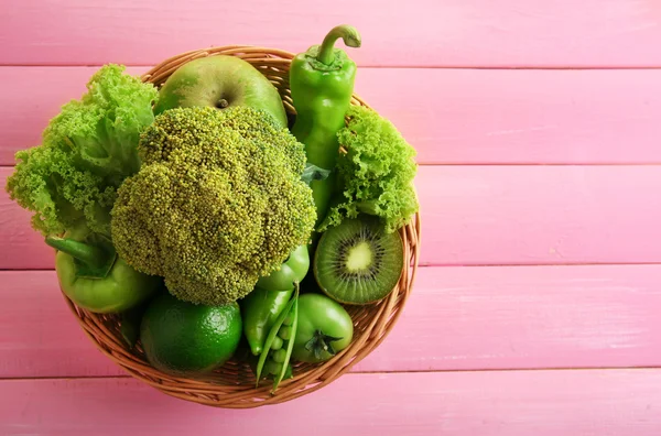 Fresh green food in wicker basket on pink wooden table, top view