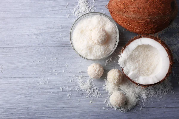 Candies in coconut flakes and fresh coconut on color wooden background