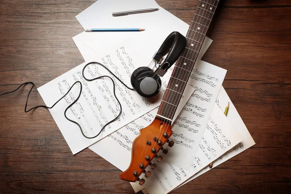 Electric guitar and headphones with musical notes on wooden background